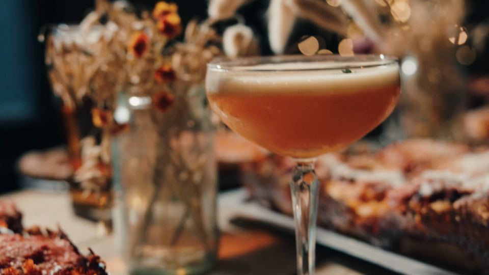 An espresso martini on a long table of Detroit and New York pizzas at The Towpath Inn, fairy lights behind