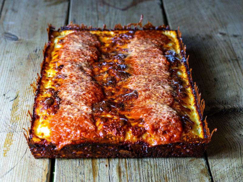 A whole Detroit-style cheese pizza with a dark caramelised cheese edge and two stripes of sauce on top