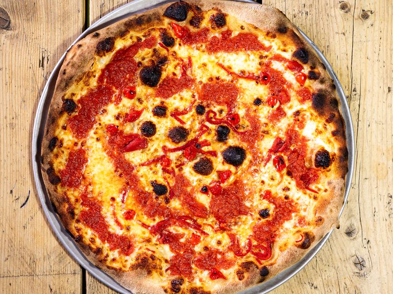 A 14-inch New York pizza with red peppers and a charred crust, from above