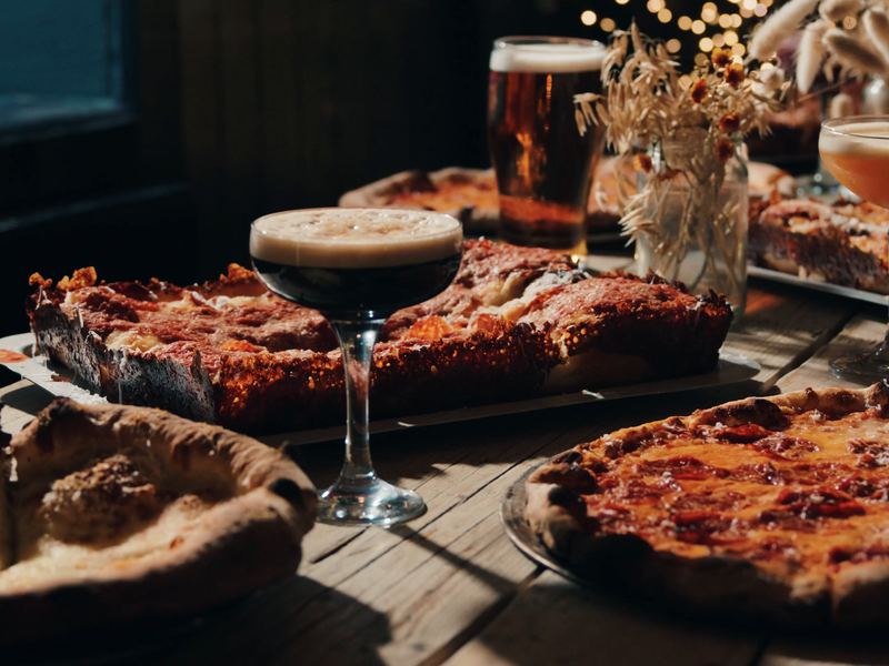 A Detroit and a New York pepperoni pizza side by side on a long table, with espresso martinis and a pint